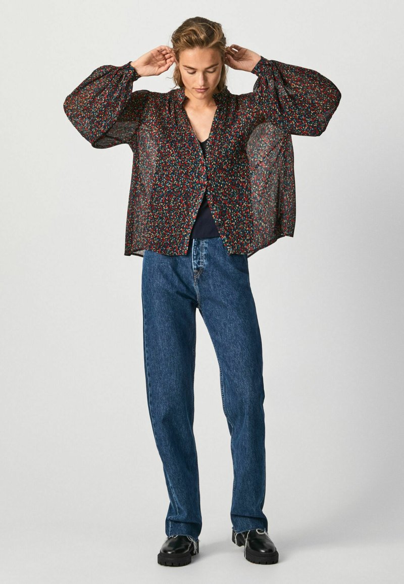 Blusa nera trasparente con motivo floreale, maniche a palloncino e chiusura a bottoni, abbinata a jeans in denim blu a vita alta.