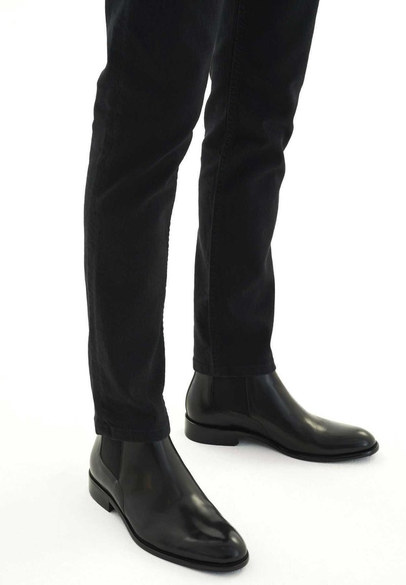 Bottines Chelsea en cuir noir avec une finition lisse, un bout arrondi, des panneaux latéraux élastiques et un petit talon carré, portées avec un jean noir.