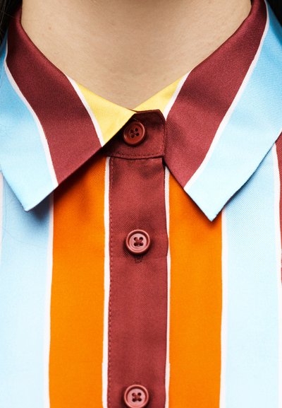 Κοντινή λήψη του γιακά και των κουμπιών πουκάμισου με κάθετες ρίγες σε χρώματα μπορντό, πορτοκαλί, ανοιχτό μπλε και κίτρινο.