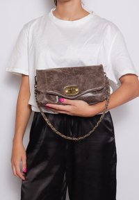 Borsa a tracolla in pelle marrone con una patta curva, dotata di una chiusura in tono dorato e una tracolla a catena. Texture liscia con una leggera grana.