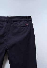 Mørkeblå chinos med fire lommer, med en lille rød og hvid flagdetalje nær taljebåndet. Glat tekstur og skræddersyet pasform.