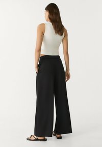 Zwarte hoge taille wijde pijpen met een elastische tailleband, gecombineerd met een aansluitend wit mouwloos topje. Minimalistisch ontwerp zonder versieringen.