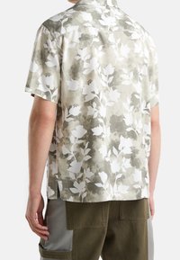 Camicia a maniche corte in un leggero grigio con motivo floreale bianco, caratterizzata da una vestibilità rilassata, tessuto morbido e colletto standard.