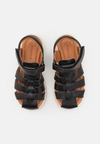 Mustat nahkaiset sandaalit, joissa on useita hihnoja, avoin muotoilu ja säädettävä nilkkahihna; vaalea sisäpohja ja valkoinen kumipohja.