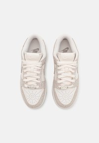 Baskets Nike avec une combinaison de couleurs beige et crème, en cuir et en mesh, à bout rond, avec des détails perforés et des lacets plats.