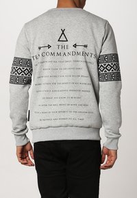 Gray sweatshirt featuring a printed design on the back with text and geometric patterns on the sleeves. Ribbed hem and cuffs.