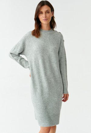 Šedé oversized svetr šaty vyrobené z měkké pleteniny, s dlouhými rukávy, ribbovaným lemem a knoflíkovými detaily na rameni.