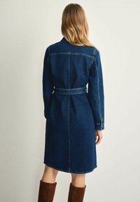 Granatowa sukienka dżinsowa z paskiem w talii, długimi rękawami i kołnierzykiem. Posiada detal w kształcie yoke z tyłu oraz długość do kolan.