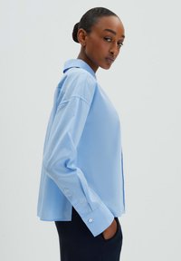 Camicia azzurra chiara con colletto, realizzata in un tessuto morbido, caratterizzata da maniche lunghe, polsini abbottonati e un fit rilassato, con orlo dritto.