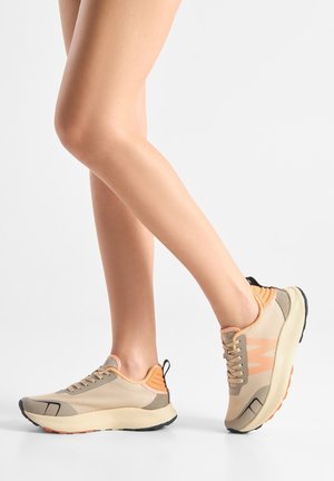 Beige athletic shoes with mesh upper and orange accents. Feature a rounded toe, textured sole, and a pull tab at the heel.