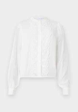 Blouse blanche à manches longues avec un col rond, dotée d'un panneau central en dentelle et d'une fermeture à boutons, ainsi que de manches froncées aux poignets.