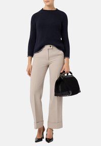 Maglione tricot blu navy con scollo rotondo, pantaloni beige su misura e borsa nera texture. Tacchi neri lucidi completano l'outfit.