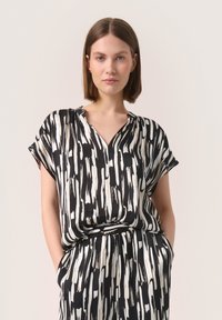 Rochie cu pattern alb-negru, cu mâneci scurte, decolteu în V și talie elastică, confecționată dintr-un material fin și ușor.