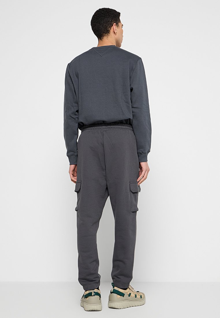 Grå sweatshirt med v-ringning och långa ärmar, kombinerad med grå cargobyxor som har sidofickor och elastisk midja, bärs med beige sandaler.