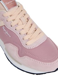 Baskets roses combinant daim et tissu, forme arrondie, détails texturés, lacets crème avec logo sur le côté.