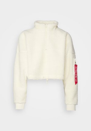 Hvit kort fleece-pull med høy krage, halv-glidelås foran, snor i kanten og en rød merkelapp på venstre erme. Myk tekstur.