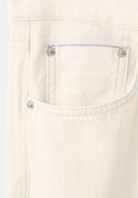 Nærbillede af lomme på off-white denimjeans med metalnitter og synlige syningsdetaljer.