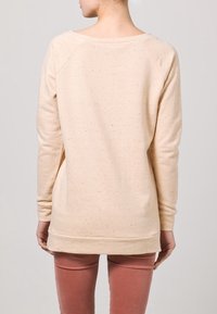 Světlé béžové tričko s texturovaným úpletem, širokým výstřihem a dlouhými rukávy, končící v oblasti boků. Zvýrazněno jemnými skvrnkami.