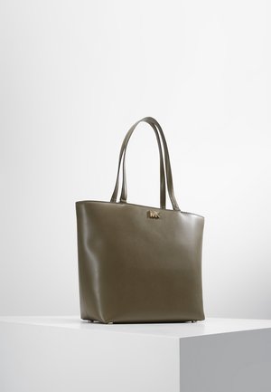 Torba typu tote z oliwkowej skóry z podwójnymi uchwytami i małym złotym logo "MK" z przodu, prezentowana na białym cokole.