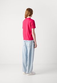Camiseta rosa de manga corta combinada con jeans de mezclilla ligeros y holgados en un tono azul claro. Los jeans cuentan con bolsillos traseros y una silueta relajada.