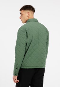 Gequiltede groene jas met een kraag, drukknoopmanchetten en een gestructureerd oppervlak; bevat een achteraanzicht dat diamantpatronen toont.