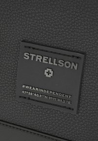 Črn razporeden material z izboklim črnim napisom. Napis vključuje besedilo "#WEARINDEPENDENT" in koordinate spodaj.