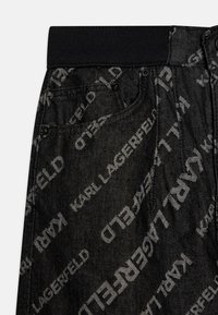 Black denim pants featuring an all-over Karl Lagerfeld logo pattern in grey, with a black elastic waistband and side pockets.