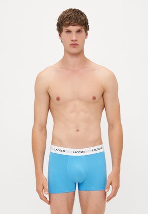 Blaue Baumwoll-Boxershorts mit einem weißen Bund, der das Lacoste-Logo trägt. Glatte Textur und enganliegendes Design für optimalen Komfort.