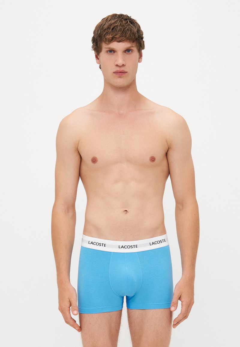 Boxer-briefs en coton bleu avec une taille blanche arborant le logo Lacoste. Texture lisse et design ajusté pour un confort optimal.