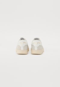 Graue und weiße Wildledersneaker haben eine cremige Sohle, eine abgerundete Zehe und eine geprägte Logodetail auf der Ferse. Das Design ist minimalistisch.