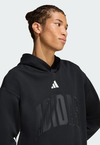 Czarna bluza z kapturem z dużym logo "ADIDAS" w teksturowanym wzorze, wykonana z miękkiego materiału, z podszytym kapturem i kontrastowym białym logo na piersi.