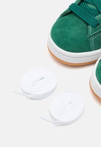Baskets en suède vert avec des semelles et des lacets en caoutchouc blanc. Les baskets présentent un bout arrondi et des détails de couture contrastants.