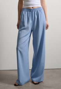 Helle blaue weit geschnittene Hose mit elastischem Bund und Kordelzug. Sie bestehen aus einem glatten Stoff und zeichnen sich durch ein entspanntes Design in voller Länge aus.
