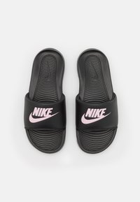 Des sandales à glisser noires de Nike avec un semelle texturée, une large sangle avec un logo rose et un design simple et plat pour un enfilage facile.