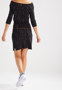 Svart off-shoulder klänning med trekvartslånga ärmar, med ett subtilt prickigt mönster och en fåll som sträcker sig ovanför knäet.