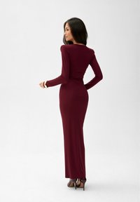 Dlouhý, přiléhavý šaty v hluboké burgundské barvě, vyrobené z hladkého materiálu, s elegantním siluetou a kulatým výstřihem.