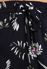 Shorts en tissu bleu marine avec un imprimé floral blanc et vert, dotés d'une ceinture élastique et d'un cordon de serrage avec embouts métalliques.