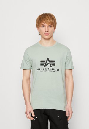 Világoszöld pamut póló, fekete logóval és "ALPHA INDUSTRIES" felirattal a mellkason, rövid ujjú és kerek nyakú kialakítás.