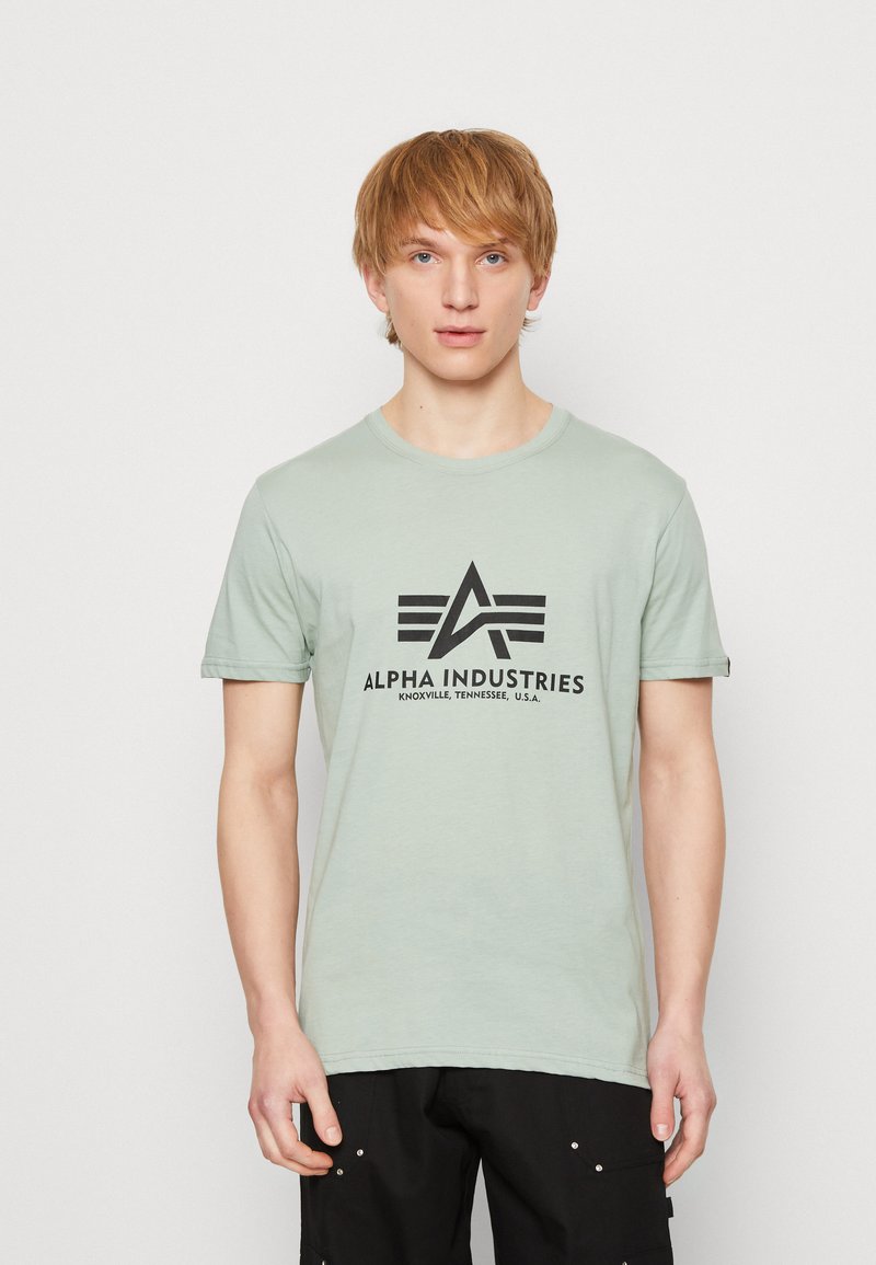 Svijetlozelena pamučna majica s crnim logotipom i natpisom "ALPHA INDUSTRIES" preko prsa, kratkim rukavima i dizajnom s okruglim izrezom.