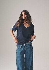 Marineblauw T-shirt met korte mouwen en V-hals, gecombineerd met hooggetailleerde losse blauwe jeans met contrasterende stiksels en een knoopsluiting.