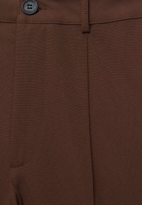 Bruine stoffen broek met een soepele textuur, een enkele zwarte knop en een frontzak met nette stiksels.