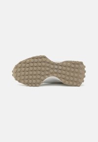 Zapatilla deportiva blanca con una suela de goma beige texturizada que presenta patrones de tracción circulares y rectangulares. Material superior suave.