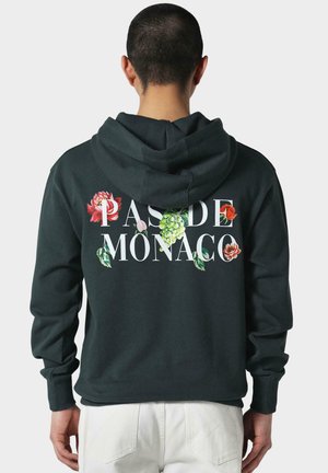 Haut à capuche vert foncé avec le texte blanc "PAS DE MONACO" et des graphiques floraux en rouge, rose et vert. Tissu doux et capuche avec cordon de serrage.