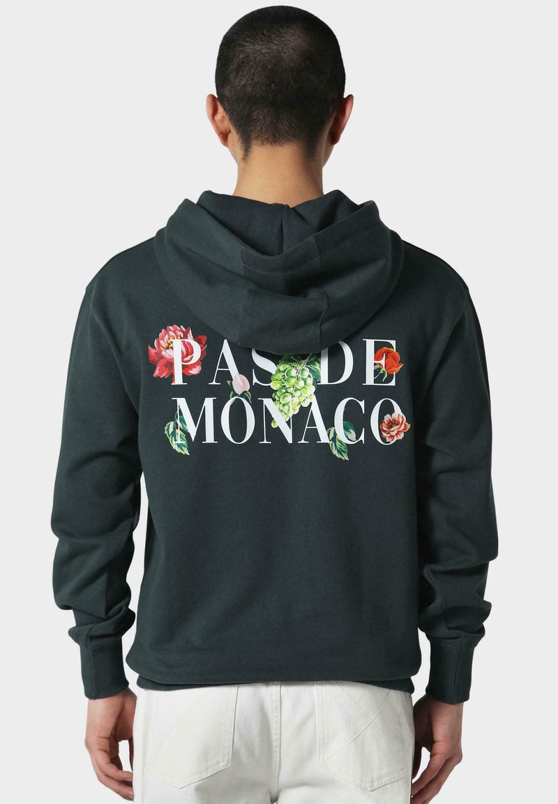 Tmavo zelená mikina s kapucňou s bielym textom "PAS DE MONACO" a kvetinovými grafikami v červenej, ružovej a zelenej farbe. Mäkka látka a kapucňa so šnúrkou.