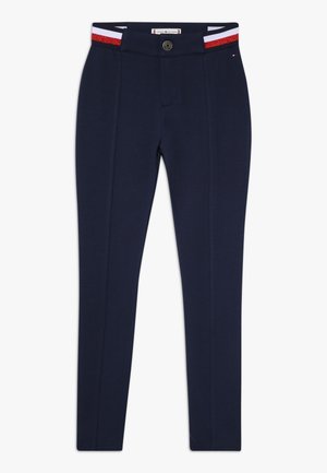 Granatowe spodnie slim fit z przednim szwem, zapięciem na guzik oraz czerwoną, białą i niebieską elastyczną gumą w pasie.