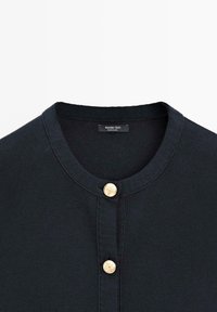 Sort strikket cardigan med rund halsudskæring og to gyldne dekorative knapper på frontklappen, mærket lyder Massimo Dutti.