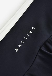 Gros plan sur un tissu noir avec le texte blanc « ACTIVE » et un logo triangulaire blanc près d'une couture blanche cousue.