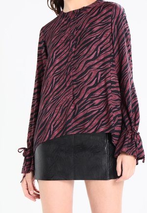 Woman wearing a long-sleeve purple and black zebra print blouse with tie cuffs and a black textured mini skirt.