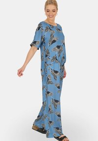 Niebieski, luźny strój wykonany z gładkiego materiału, z czarnym wzorem liści. Krótkie rękawy i szerokie spodnie o swobodnej sylwetce.