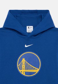 Hoodie azul feito de uma mistura de algodão, com um logótipo redondo de uma ponte em amarelo, e um swoosh branco da Nike acima do logótipo.
